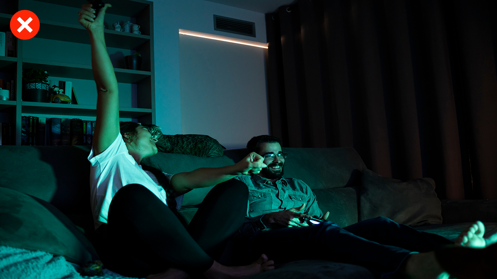 Zwei Personen sitzen im Dunkeln auf dem Sofa und schauen TV. Das Bild ist sehr dunkel und hat einen grünlichen Farbton.
