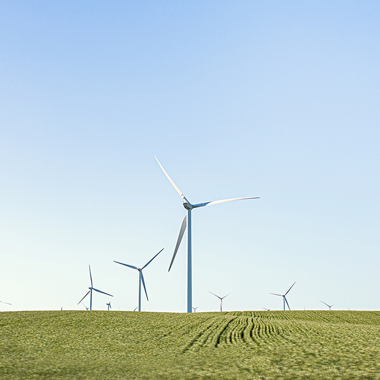 Windkraftanlagen stehen auf einem grünen Feld unter einem klaren, blauen Himmel.