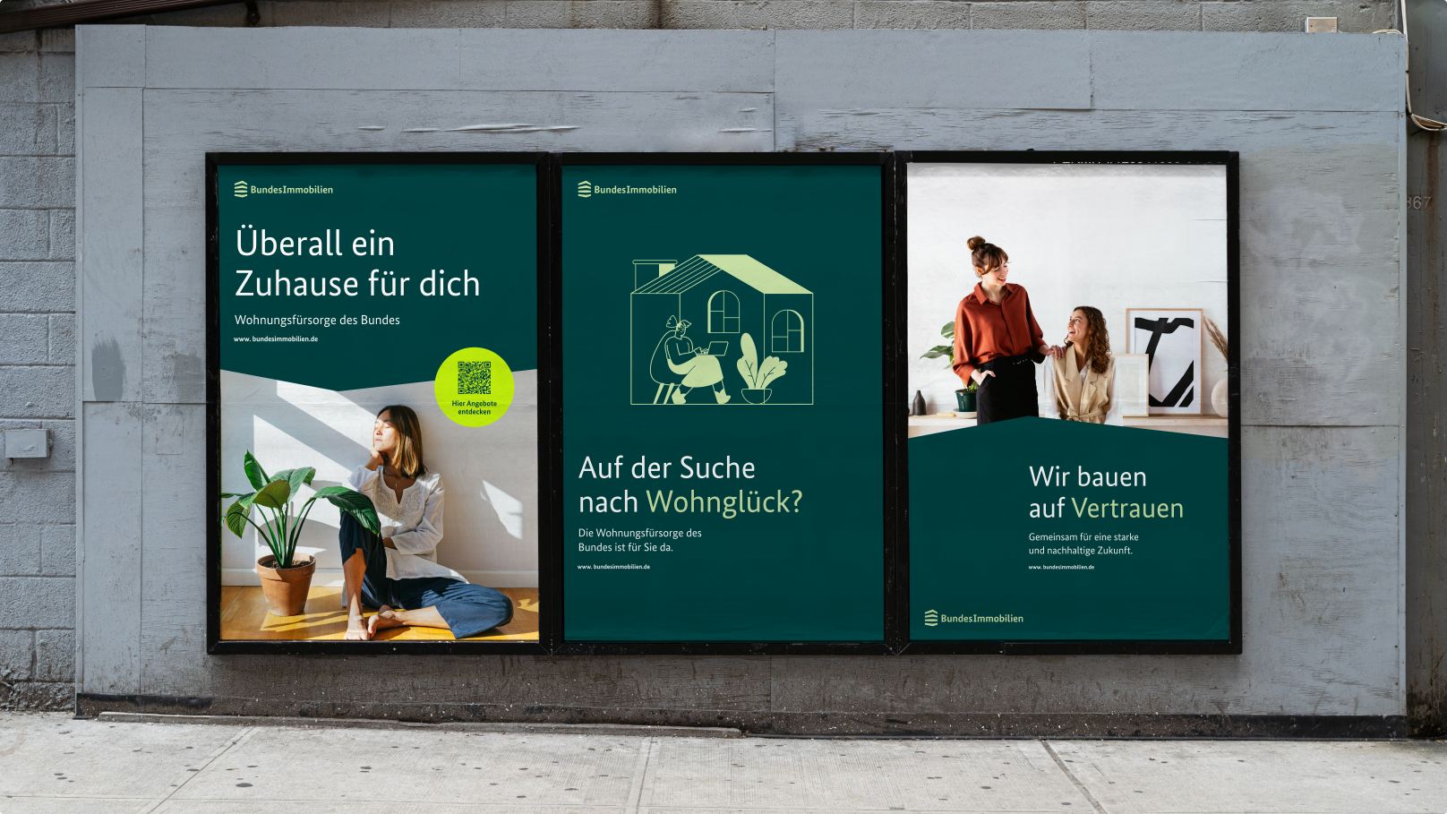 Drei Werbeplakate an einer Wand. Sie zeigen Slogans wie "Überall ein Zuhause für dich", "Auf der Suche nach Wohnglück?" und "Wir bauen auf Vertrauen".